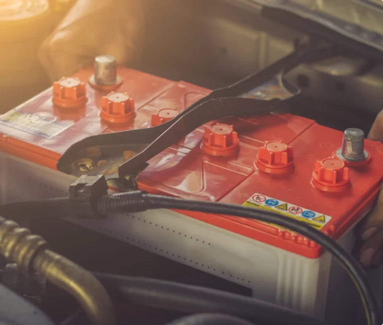 Rött bilbatteri monterat i motorrum. Vi utför kontroll och byte av bilbatteri.