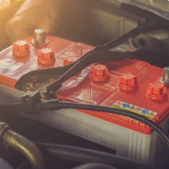 Rött bilbatteri monterat i motorrum. Vi utför kontroll och byte av bilbatteri.